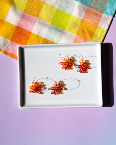 red orange flower hoop earrings in silver and gold on tray
