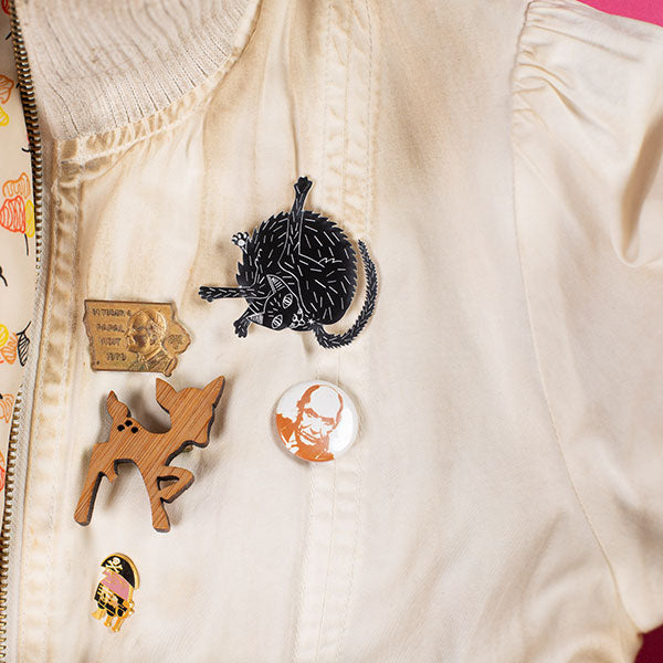 black cat pin shown on jacket with other pins