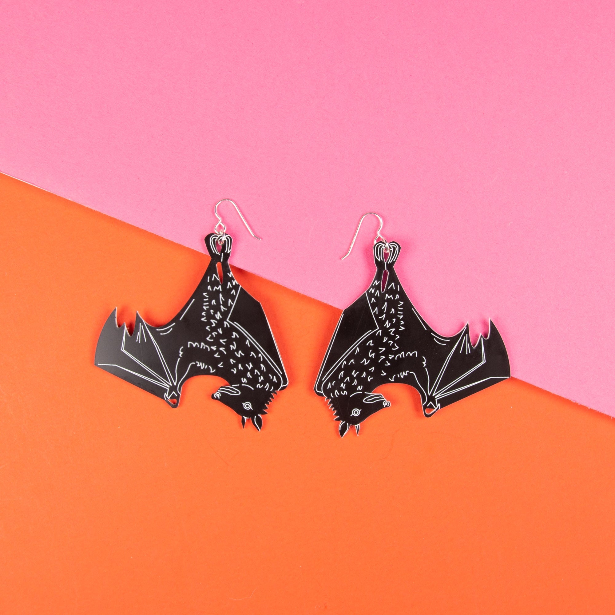 Large black bat earrings shown on pink and orange background