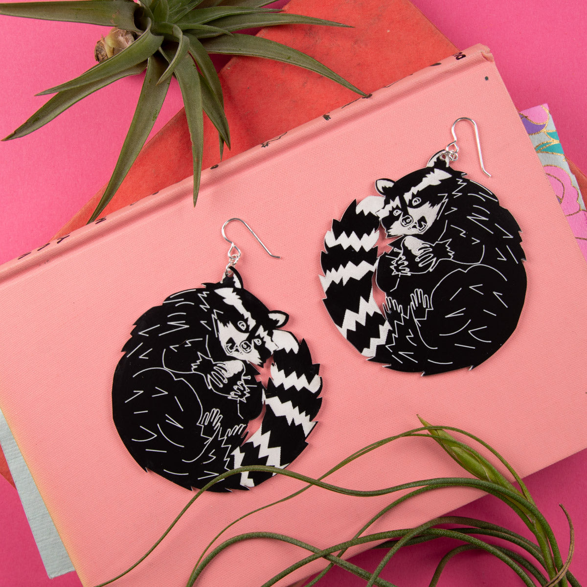 Large black and white raccoon earrings on top of pink book.