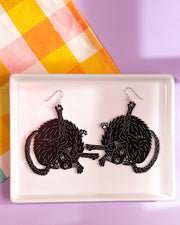 Large black cat earrings on white tray. Cats licking butts
