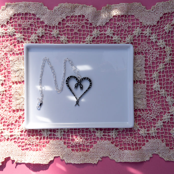 Heart of Snakes Necklace on white tray atop pink background