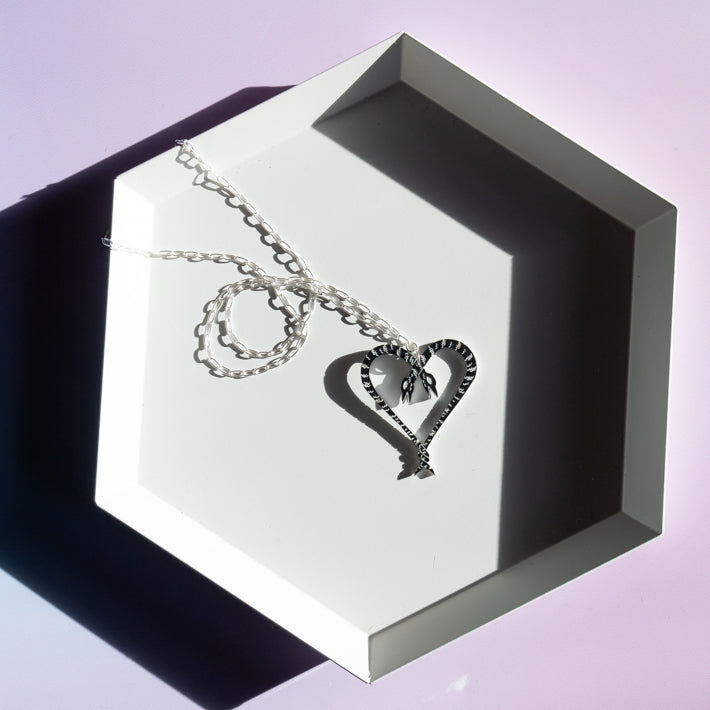 Heart of Snakes necklace on hexagonal tray with stark shadows