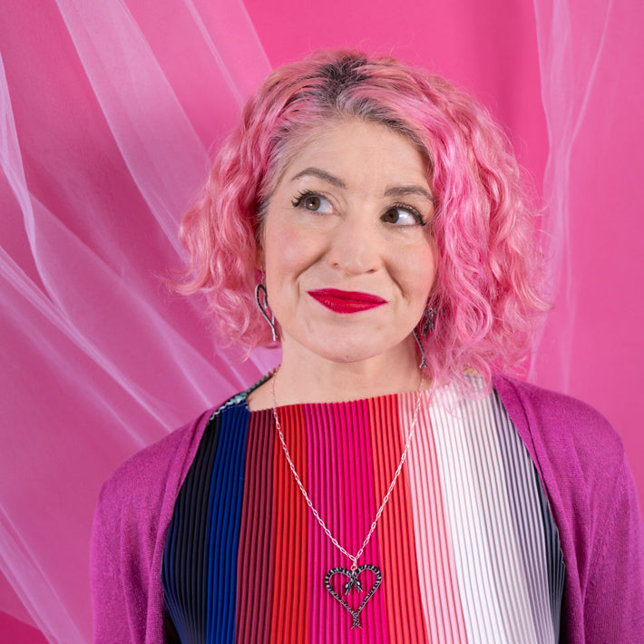 Model with pink hair and colorful top wearing heart of snakes necklace