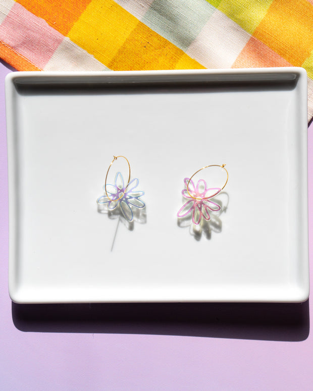Iridescent flower earrings with gold hoops on white tray