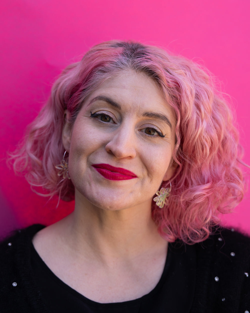 Model with pink hair wearing iridescent flower hoop earrings 