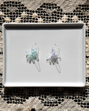 Iridescent flower silver hoop earrings on white tray