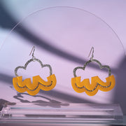 Orange and silver cloud earrings hanging from clear acrylic against a purple background