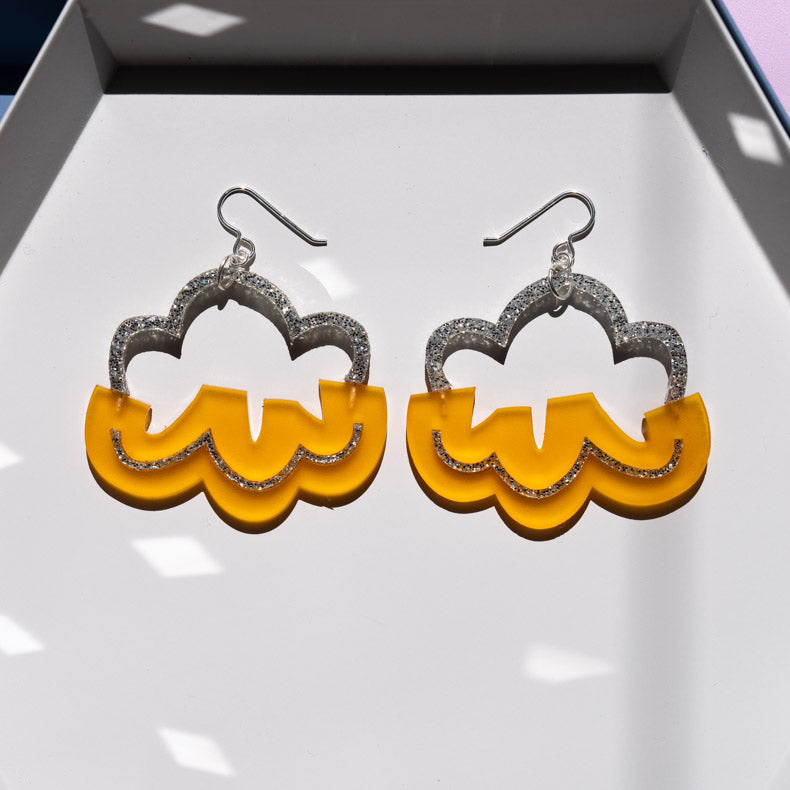 Orange and silver cloud earrings on a white tray. 