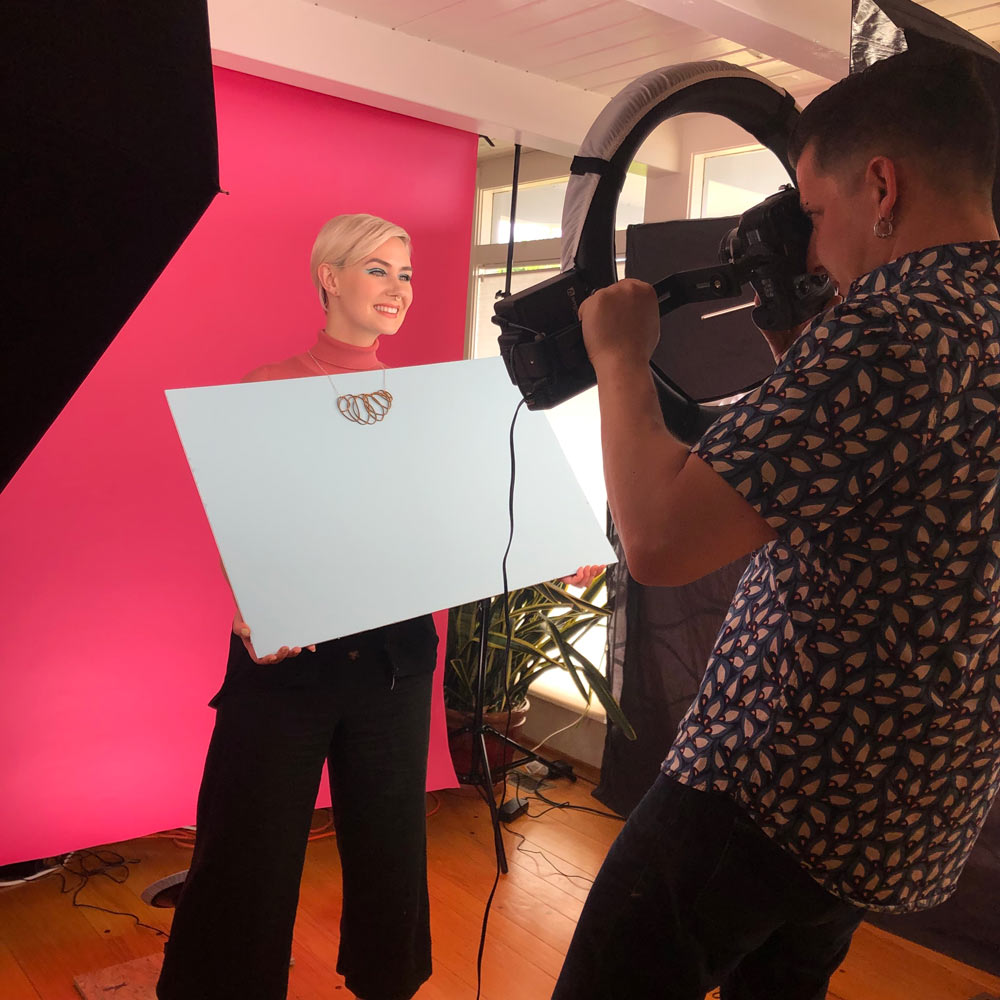 Blonde woman modeling a necklace for a photographer.