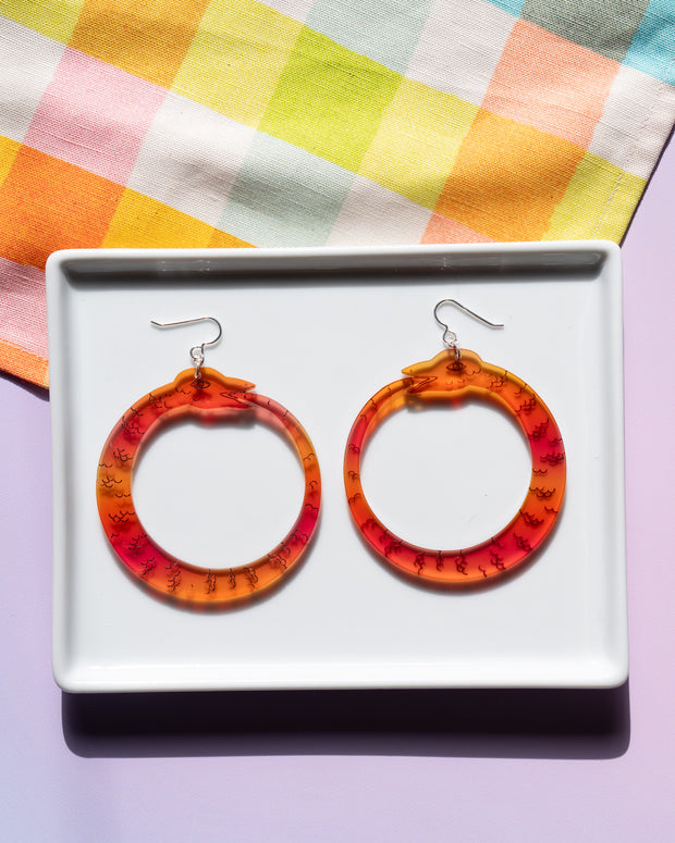 red orange ouroboros earrings on white tray on top colorful background