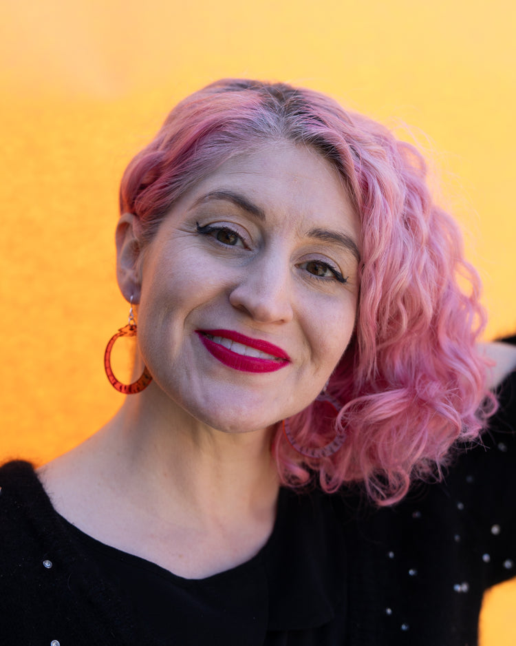Model with pink hair wearing red orange ouroboros earrings in front of yellow wall