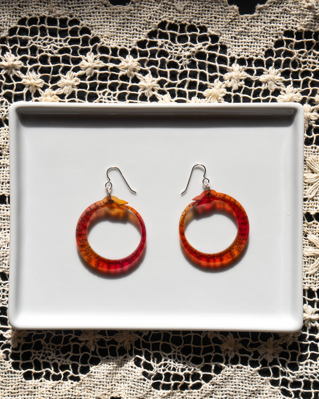 small red orange ouroboros earrings on white tray