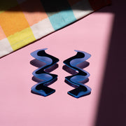 Zigzag blue acrylic earrings shown over pink background