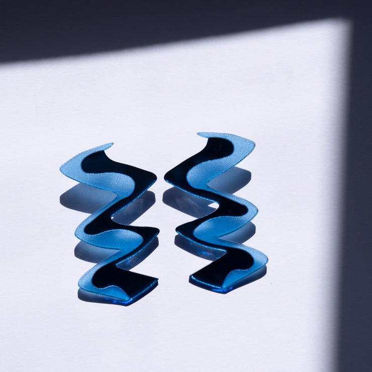 Zigzag blue acrylic earrings shown over white background with shadows