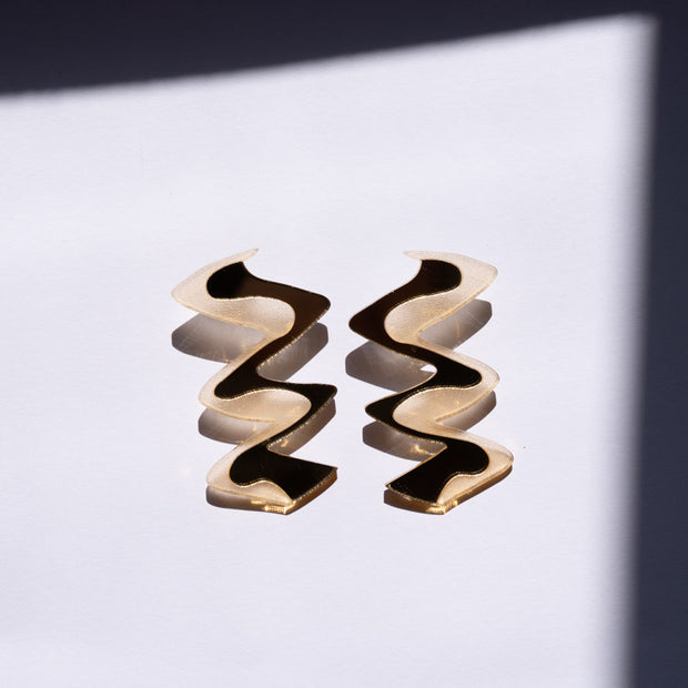 Zigzag gold acrylic earrings shown near window