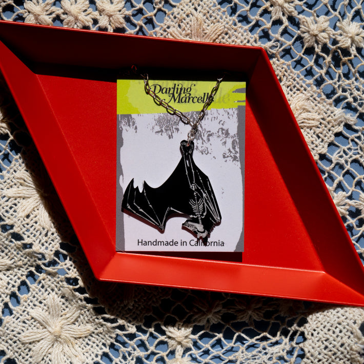 black and white bat skeleton necklace on necklace card atop red tray