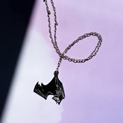 black and white bat skeleton pendant on a silver chain on a purple and white background