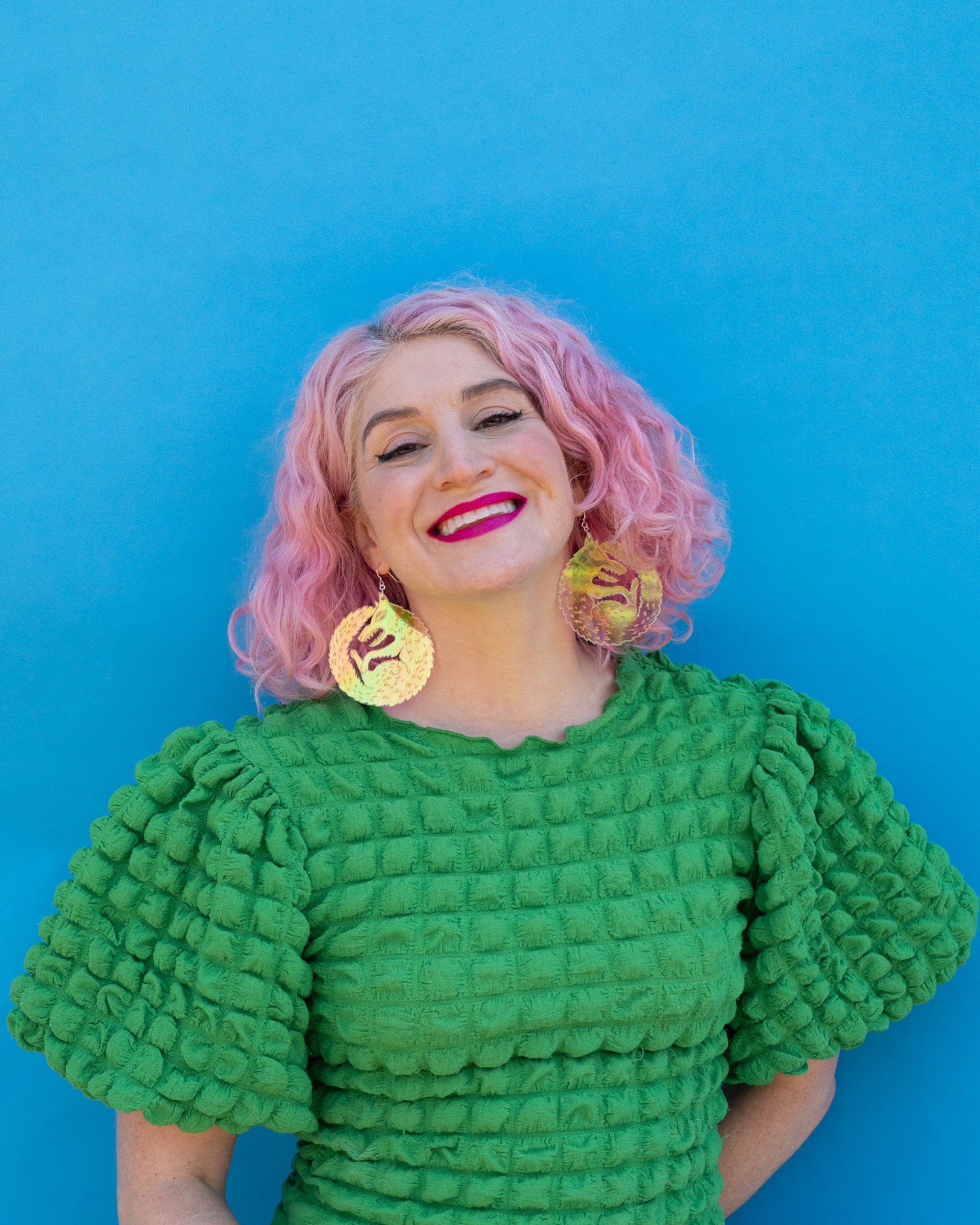 Large iridescent wolf earrings on model with pink hair against a blue background