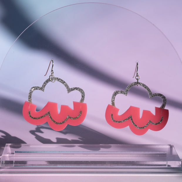 pink cloud earrings hanging on clear sheet with purple background