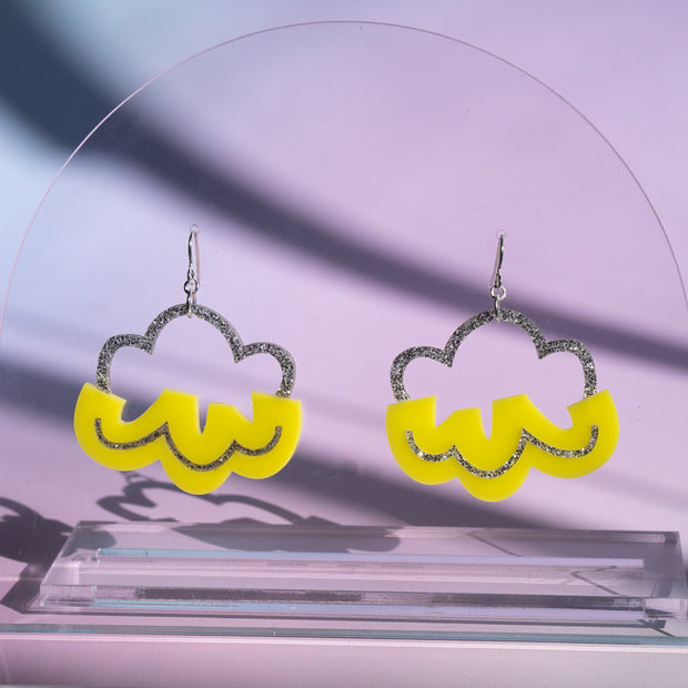 Silver and yellow cloud earrings shown on clear acrylic stand in front of a purple background
