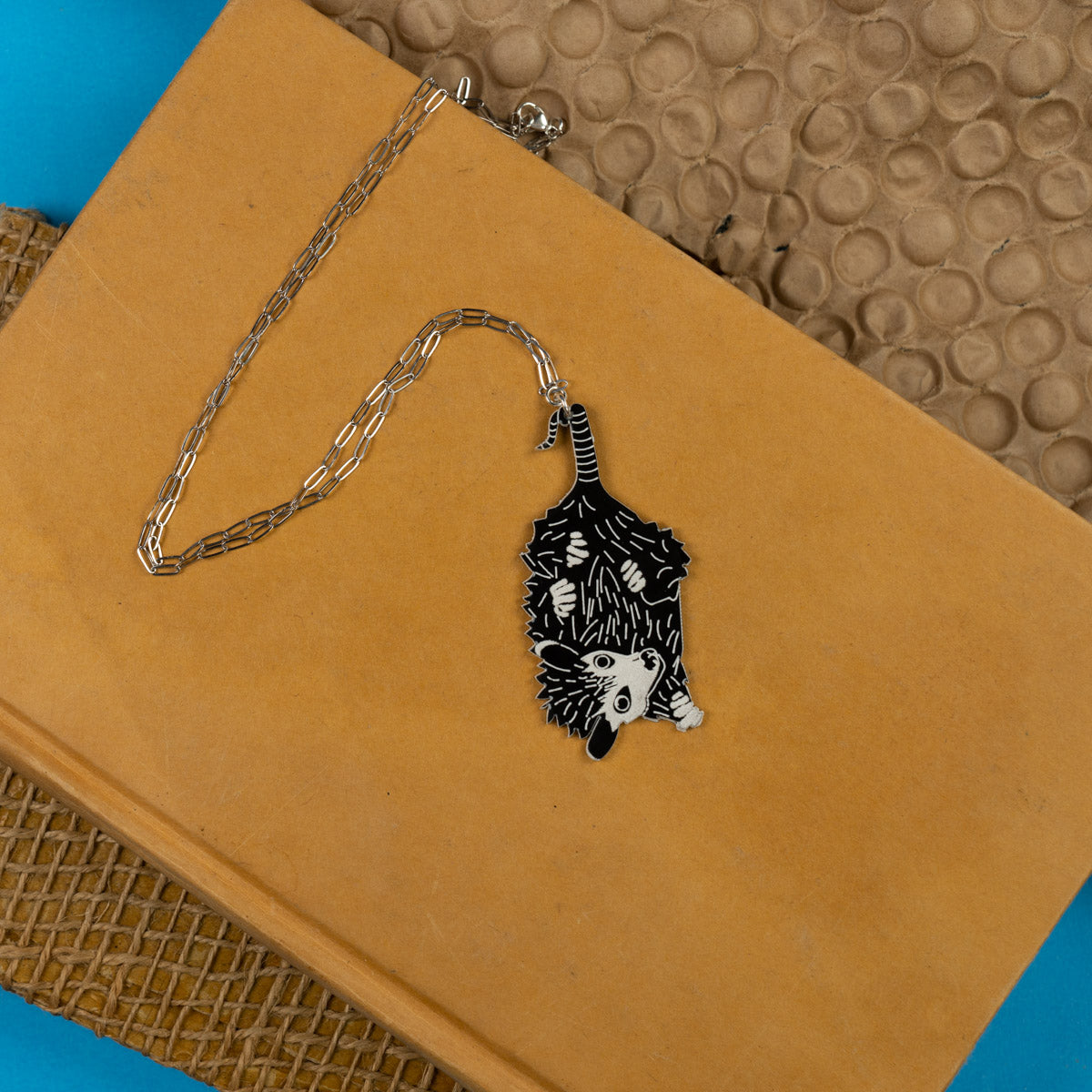 Baby possum necklace shown atop a marigold colored book