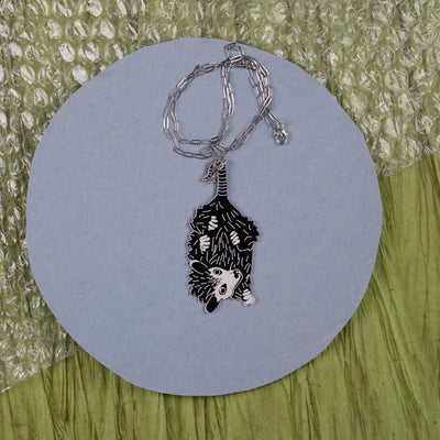 Baby Possum necklace shown on a gray and green background