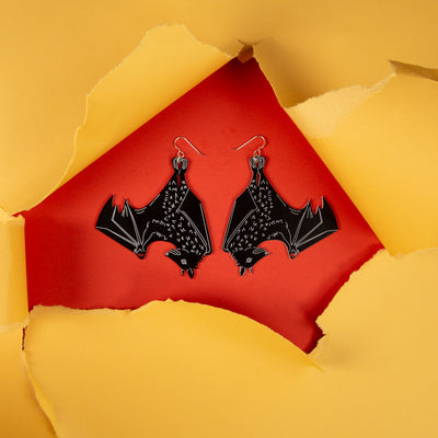 Large black bat earrings shown on orange and yellow background