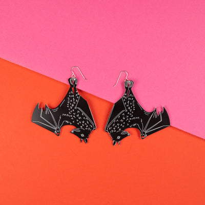 Large black bat earrings shown on top orange and pink background