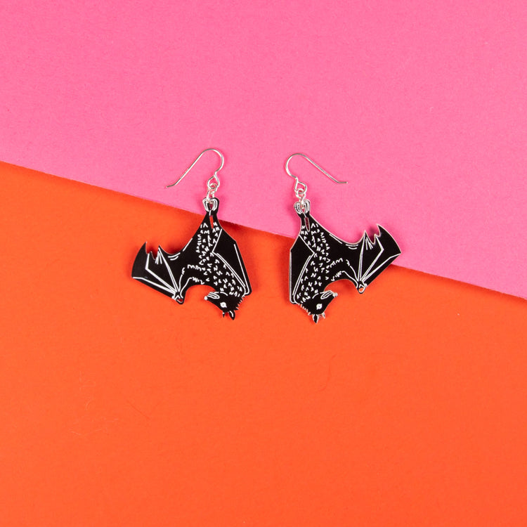 black bat earrings over pink and orange background