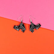 black bat earrings over pink and orange background
