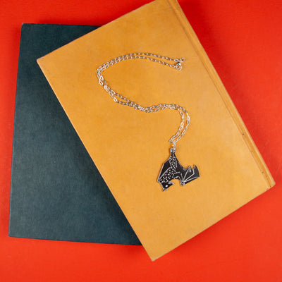Black bat necklace lying on top of books. 