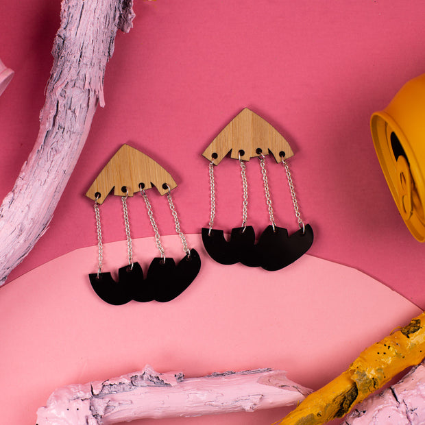 Black and wood dangle earrings over pink with props