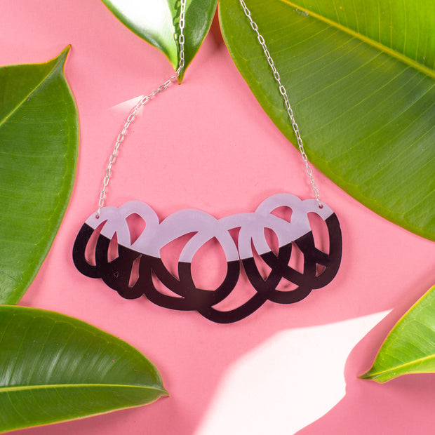 Chunky black & lilac statement necklace on pink background with green leaves