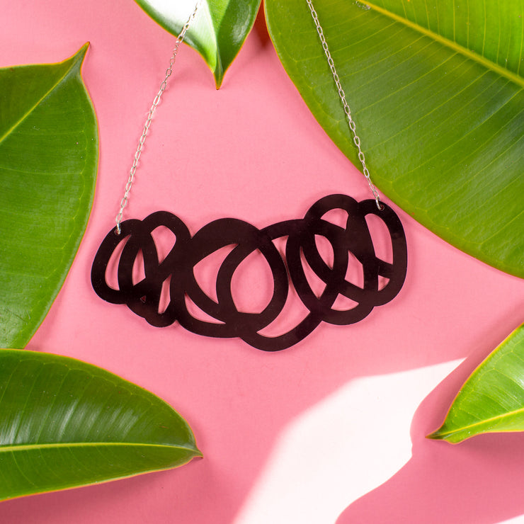 Chunky black statement necklace on pink background with green leaves