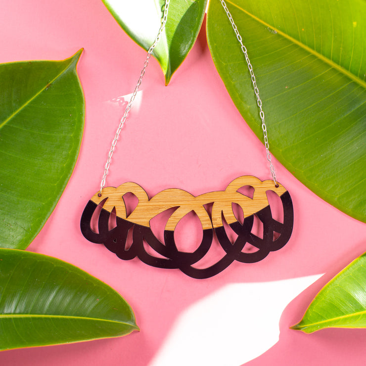 Chunky black and wood statement necklace over pink background with green leaves