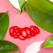 Chunky red statement necklace on pink background with green leaves