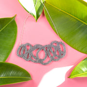 Chunky silver glitter statement necklace on pink background with green leaves