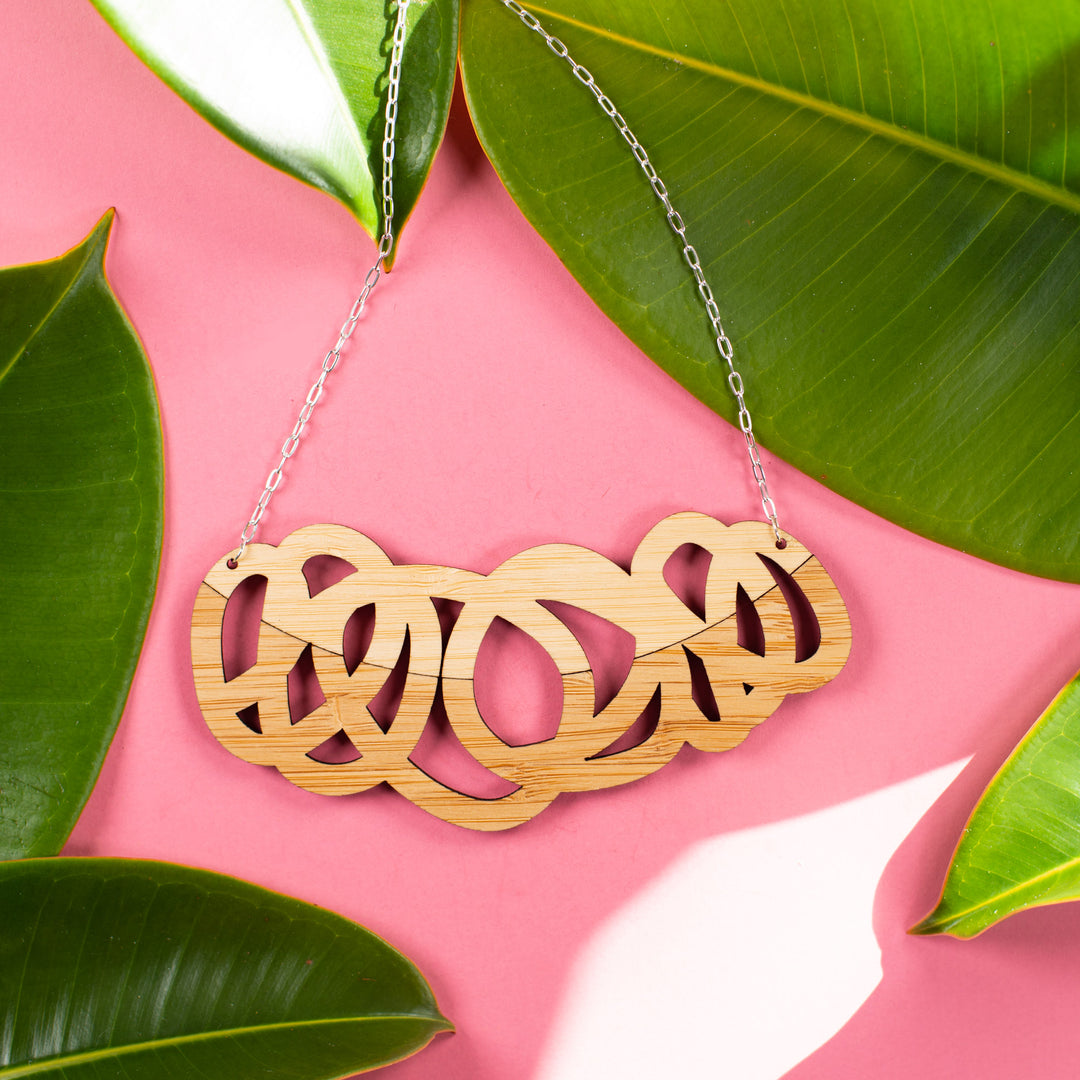 Chunky two tone wood statement necklace on pink background with green leaves