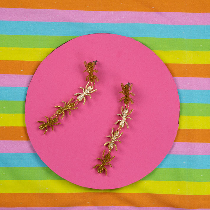 Gold ant earrings on colorful background
