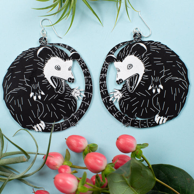 large possum earrings over blue background with plants