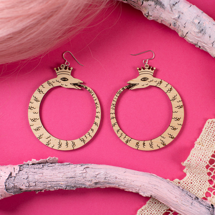 large wood ouroboros earrings over pink background