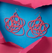 Pink statement earrings shown on contrasting blue background with torn paper