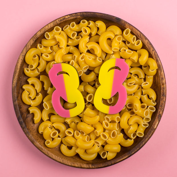Pink and yellow statement stud earrings in bowl of macaroni noodles