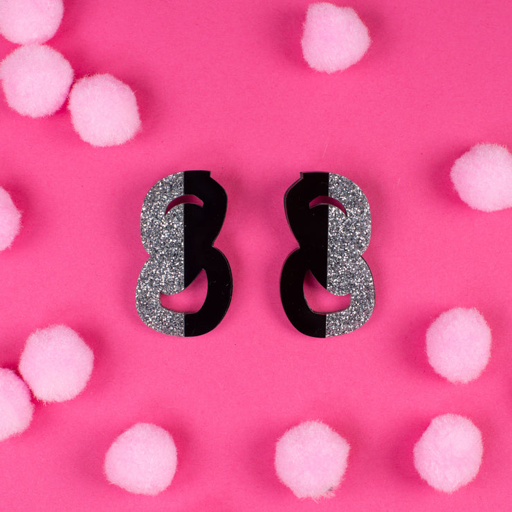 black and silver statement stud earrings on pink background