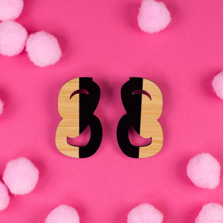 Black and wood statement stud earrings on pink background
