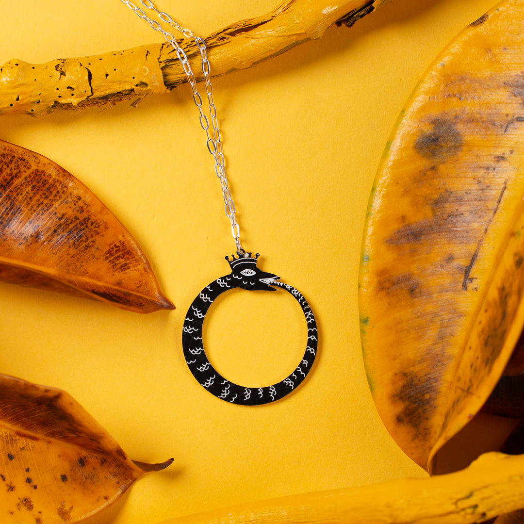 black ouroboros necklace over yellow background