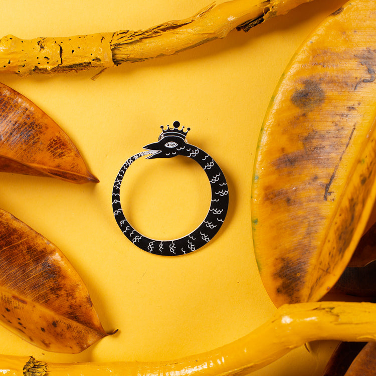black ouroboros pin over yellow background
