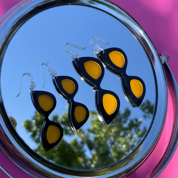 Small and large black and orange sunglass earrings on a mirror