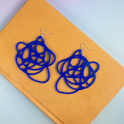 Bright blue graffiti earrings shown atop a yellow book on a blue background